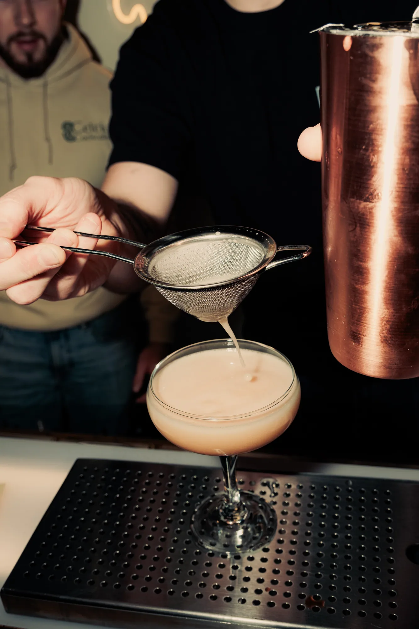 A cocktail being double-strained into a coupe