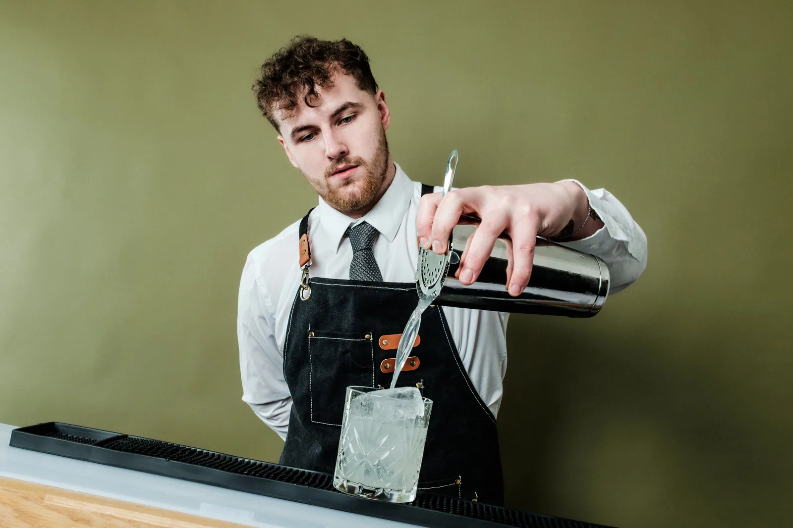 A mixologist straining a drink over ice